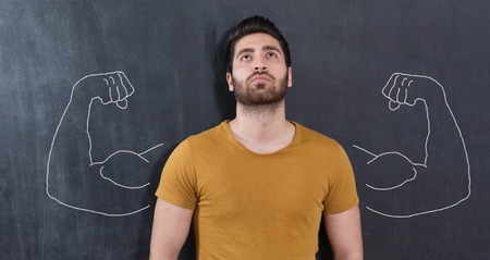 Young man against the background of depicted muscles on chalkboardの写真素材