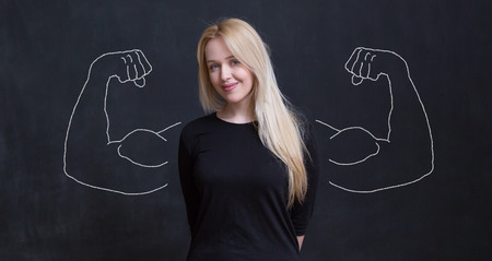 Young woman against the background of depicted muscles on chalkboardの写真素材
