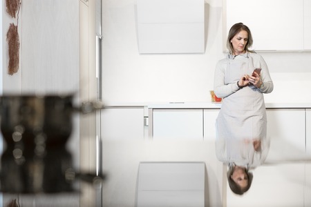 Woman texting on the phone in kitchen. Woman using technology in kitchenの写真素材