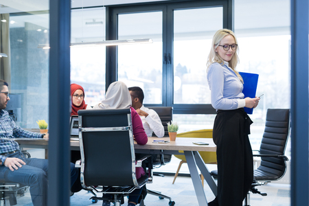 business woman standing with her staff in background at modern bright office conference roomの写真素材
