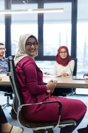 Arabian Businesswoman in office with Businesspeople meeting in the background, Arabian woman wearing Hijab in office with her colleagues in backgroundの写真素材
