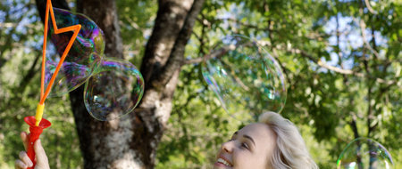 Gorgeous young brunette girl blowin soap bubbles in sunlit park.