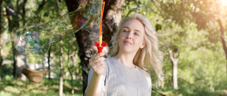 Gorgeous young brunette girl blowin soap bubbles in sunlit park.の写真素材
