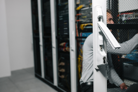 Young man is standing next to the racks with computer equipmentの写真素材