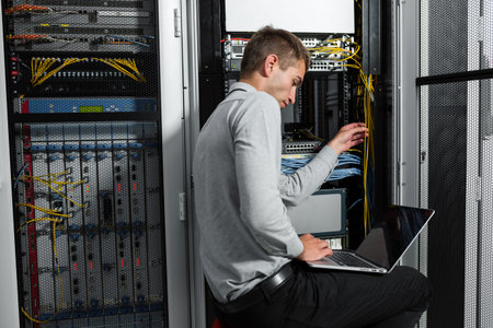 Portrait of modern young man holding laptop standing in server room working with supercomputer