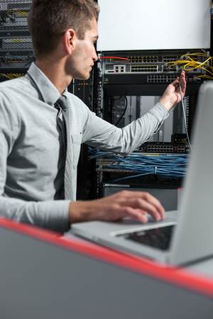 Young man is standing next to the racks with computer equipmentの写真素材