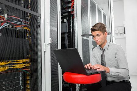 Portrait of modern young man holding laptop standing in server room working with supercomputerの写真素材