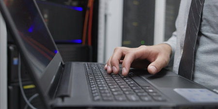 IT data specialist working on laptop on maintaining server rack