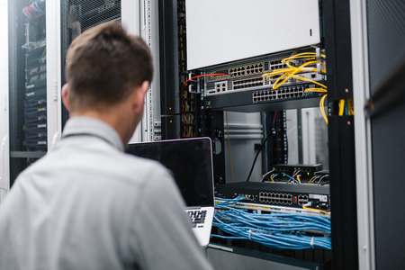 young man connecting wires in server cabinet while working with supercomputer in data centerの写真素材
