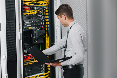 young man connecting wires in server cabinet while working with supercomputer in data centerの写真素材