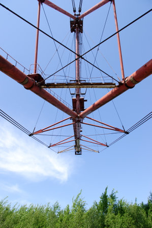 A shovel boom of a walking excavator that is pointing in blue sky over a green treesの写真素材