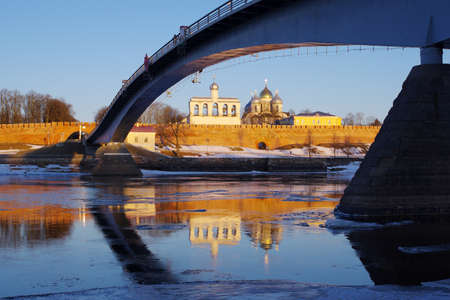 Sunrise over a medieval fortress. Belfry and Cathedral over red brick walls mirroring in a river. Velikiy Novgorod Kremlin reflecting in a Volkhov river. Fortress framed with river and bridgeのeditorial素材