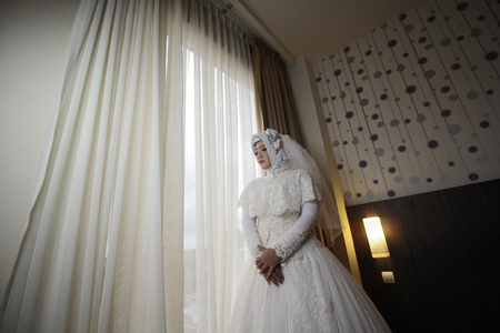 The bride wearing white wedding dress standing behind the curtainsの写真素材