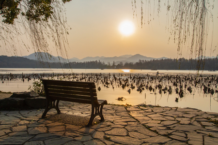 Empty bench overlooking sunset over West Lake in Hangzhou, Chinaの写真素材