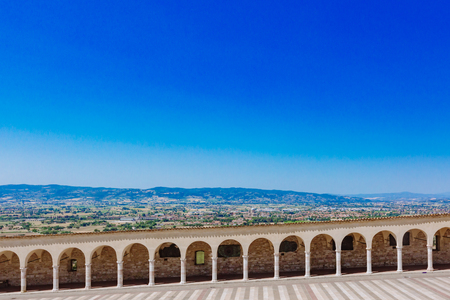 Corridor with arches and columns in the lower square of San Francis in Assisi, Italy in Assisi, Italy, with fields and landscape outside of the townの写真素材