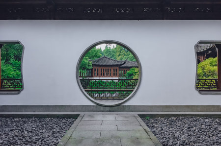 Path leading to a moon gate with view of traditional Chinese building, in a Chinese garden, near...