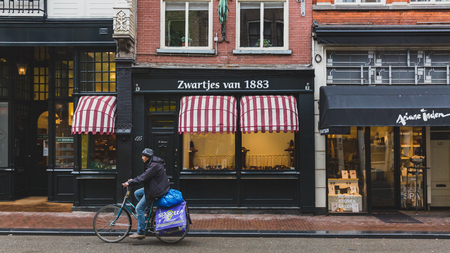 Amsterdam, the Netherlands - March 4, 2017: Local biking past shops in downtown Amsterdamのeditorial素材