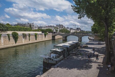 June 14, 2019 - Paris, France: People walking on the quay by Seine with cruise boat in riverのeditorial素材