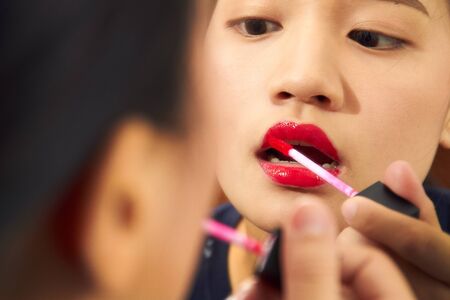 Cosmetics and makeup. Perfect lip makeup. Close up portrait of attractive girl rouging her lips. She is holding red lipstick. Her mouth is gently openの写真素材