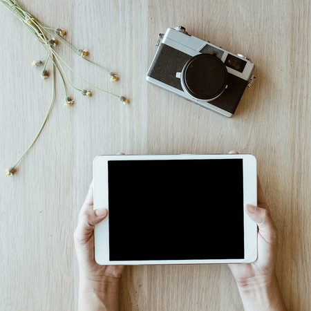 hand hold on tablet and retro camera on wooden table backgroundの写真素材