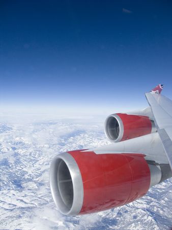 View from an aeroplane window of the red engines over some mountains with a deep blue sky.