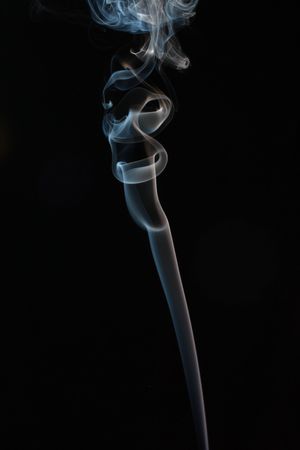 Abstract smoke trail from an incense stick against a black backgroundの写真素材