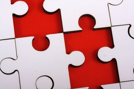 Macro shot of a plain white jigsaw puzzle with two pieces missing which show as red gaps.の写真素材