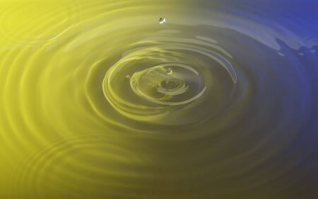 Drops of water splashing into more water creating a ripple pattern. The entire picture has a blue and yellow gradient to it.の写真素材