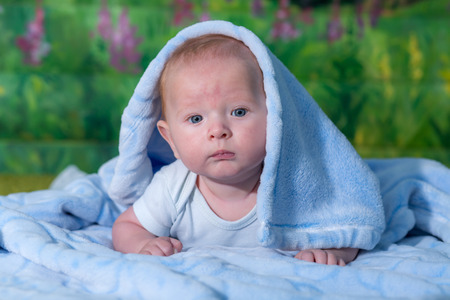 Portrait of a baby in a blue towel. On the green carpet.の写真素材