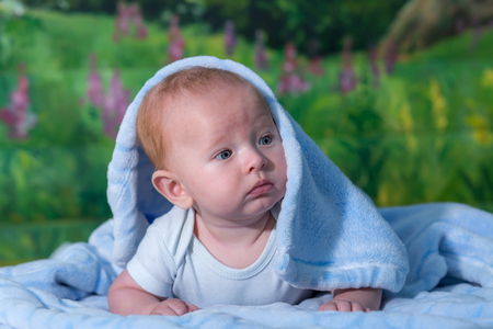 Portrait of a baby in a blue towel. On the green carpet.の写真素材