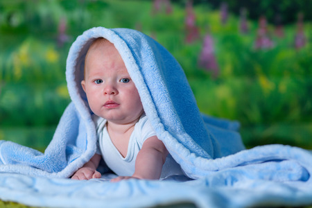 Portrait of a baby in a blue towel. On the green carpet.の写真素材