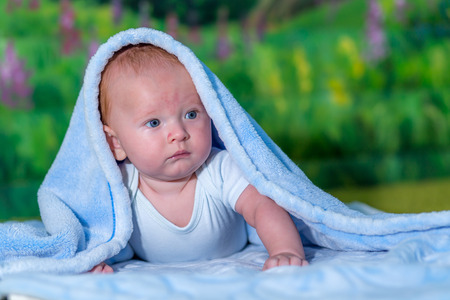 Portrait of a baby in a blue towel. On the green carpet.の写真素材