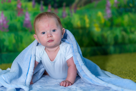 Portrait of a baby in a blue towel. On the green carpet.の写真素材