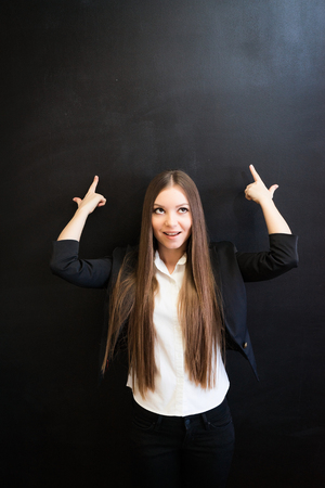 Pretty office woman pointing up to copyspace on chalkboard with thoughtful face expression. looking up.Fingers like a gun gesture, surprised face.Woman thoughts.の写真素材