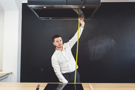 A male designer in a shirt makes measurements, measures the height of the rack, looks at the cameraの写真素材