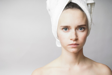 Beautiful woman with a towel on her head after a bath confidently looks at the camera. Isolated on a gray backgroundの写真素材