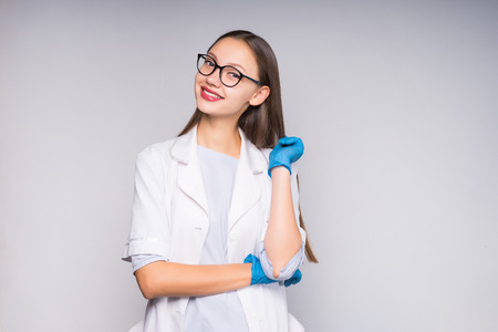 Joyful woman doctor wearing glasses, wearing robe, wearing blue gloves smiling and looking at cameraの写真素材