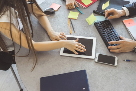 A working table during a business meeting between a man and two women. On the table are various electronic devicesの写真素材