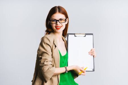 Beautiful female teacher with glasses is holding a folder with documents, smiling smtrit in the camera. Isolated on a gray backgroundの写真素材