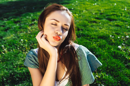 Beautiful cheerful girl on the lawn with bright green grass showing duck lipsの写真素材