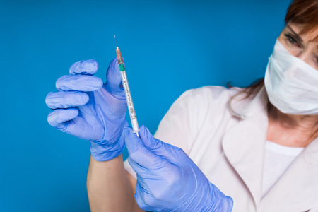 A female doctor wearing blue gloves holds a syringe in her hands, gazing intently at the syringe....