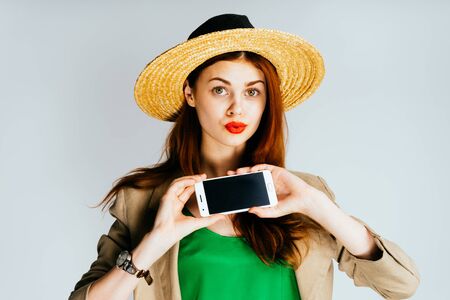 Young beautiful woman in straw hat shows phone in surpriseの写真素材