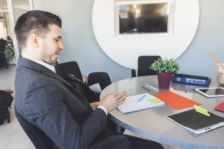 A business man in a jacket is sitting at the desk at work in the office. Side viewの写真素材