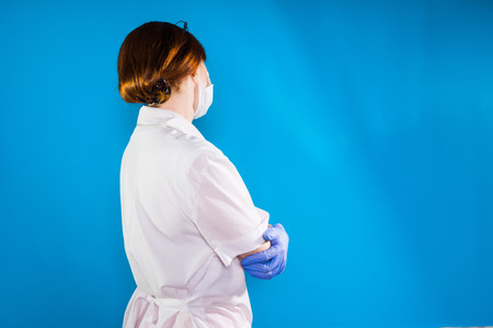 Woman doctor in white lab coat wearing blue gloves. Side view. Isolated on a blue backgroundの写真素材