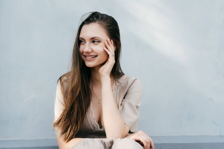 Young beautiful girl sits smiling, looks to the left, holds a hand by the faceの写真素材