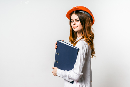 Young confident woman builder wearing a hard hat, holding a folder with drawings, smiling looking at the cameraの写真素材