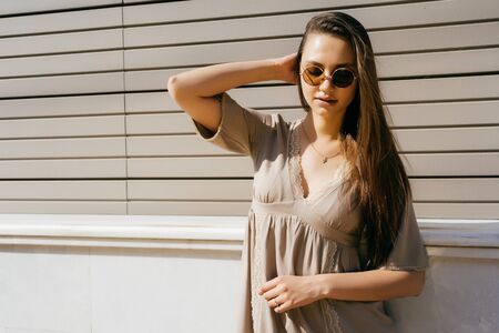 A girl in round glasses is standing in the street under the sunの写真素材