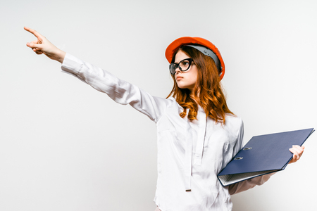 An energetic young woman builder in a helmet points points forward with a serious lookの写真素材