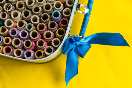 Colored thread spools in a box on a yellow backgroundの写真素材