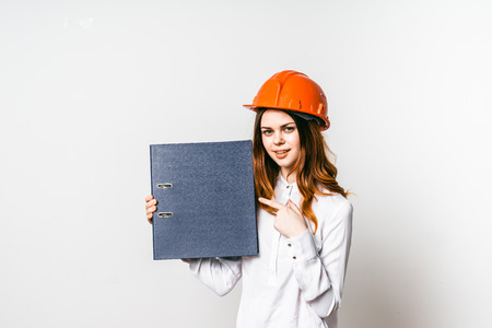 Young female construction worker in helmet holding a folder and pointing at itの写真素材